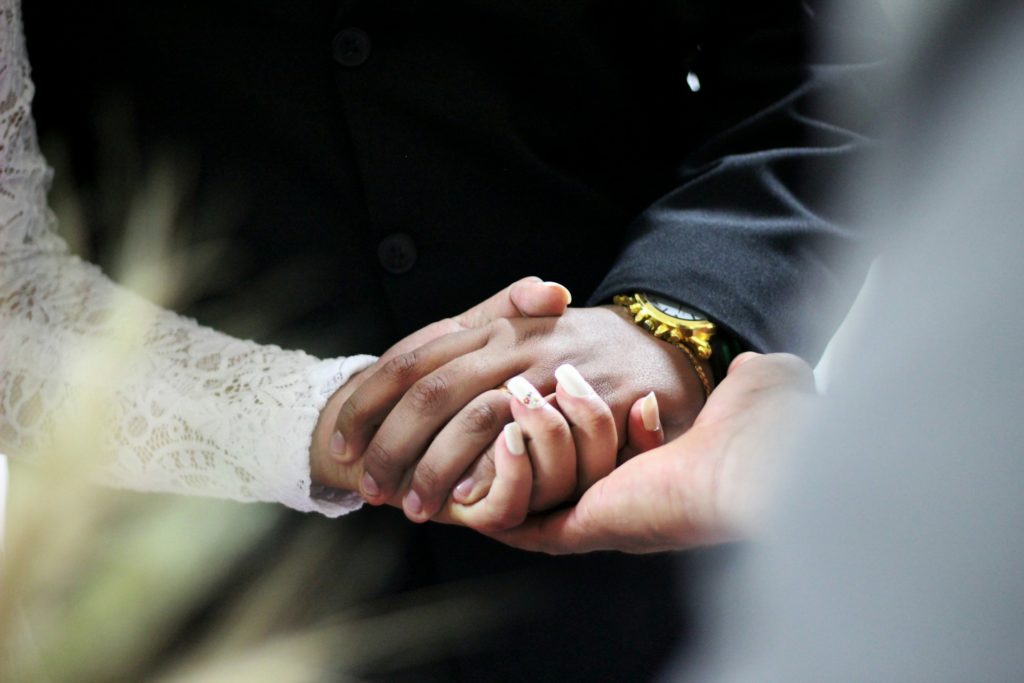 Mariés qui se tiennent la main, soutenus par celle de l'officiant de cérémonie.