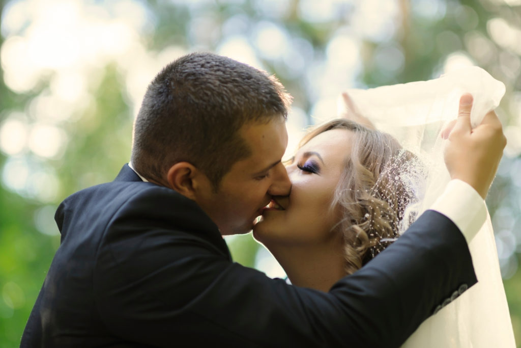 Gros plan des mariés qui s'embrassent en soulevant le voile de la mariée.