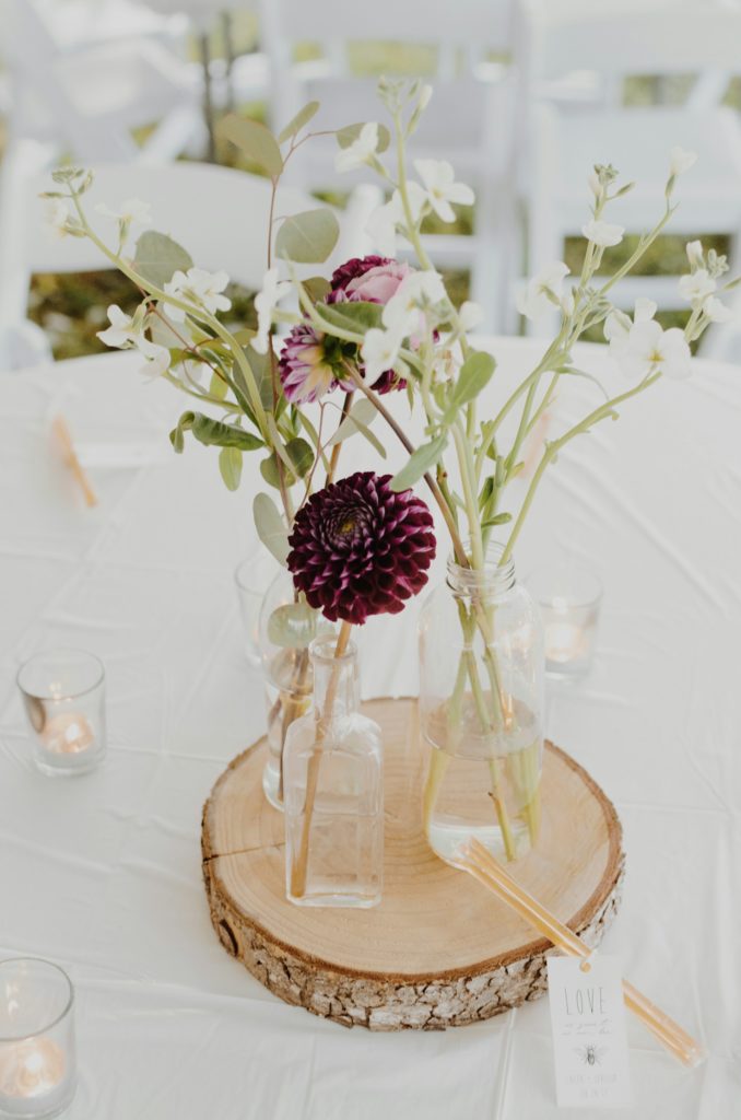 Table de mariage blanche avec fleurs bordeaux et rondin de bois.