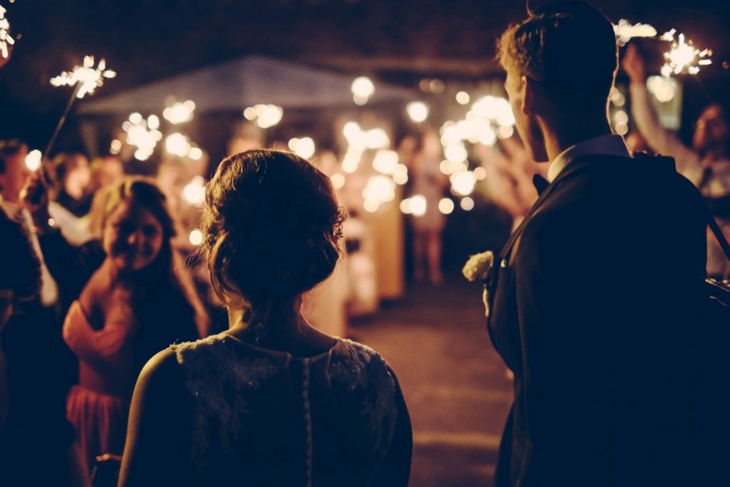 Mariés de dos dans la nuit éclairés par leurs proches qui tiennent des bougies étincelles
