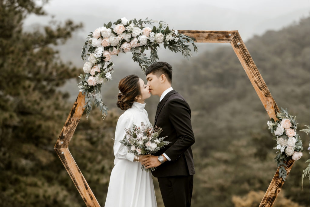 Couple de mariés qui s'embrasse devant une arche de cérémonie octogonale en bois
