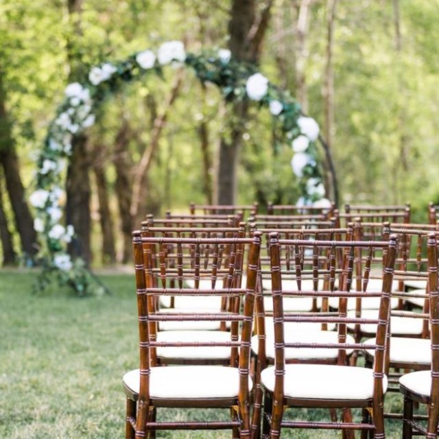 Chaises en bois alignées pour une cérémonie laïque de mariage avec l'arche en arrière plan